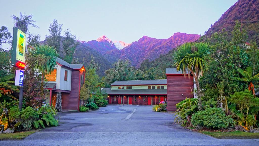 a building with palm trees and mountains in the background at Punga Grove in Franz Josef