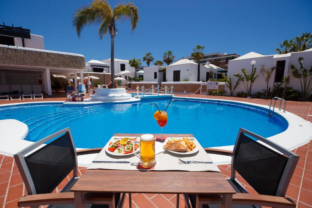 a table with food and drinks next to a swimming pool at Los Cardones Boutique Village in Playa de las Americas