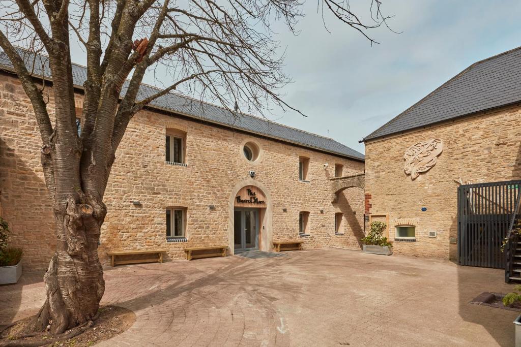 un grand bâtiment en briques avec un arbre devant lui dans l'établissement The Barrel Store Cirencester, à Cirencester