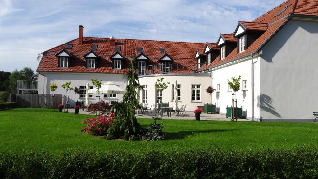 White inn with red tile roof, outdoor terrace tables and umbrellas, neatly trimmed lawn.