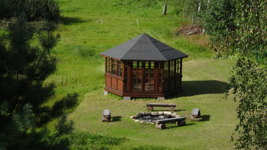 Octagonal wooden gazebo on a grassy clearing beside a circular firepit with log benches.