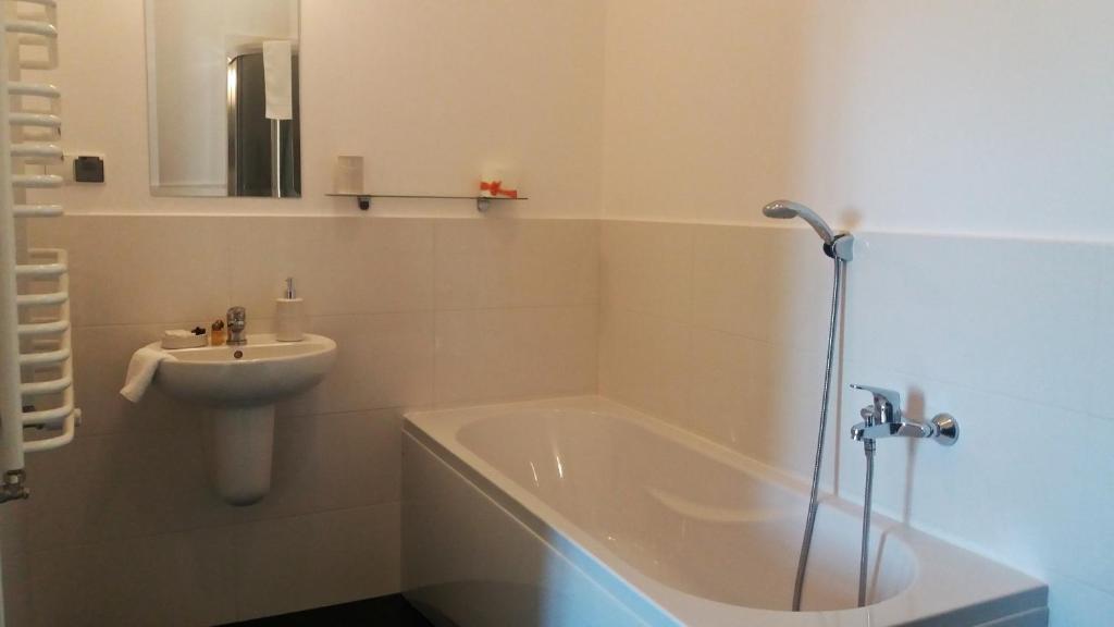 Bright tiled bathroom with bathtub, handheld shower, pedestal sink and small mirror, clean minimalist atmosphere.
