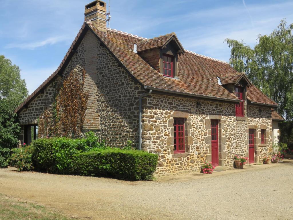 uma antiga casa de pedra com janelas com persianas vermelhas em Gite des Basses Touches em Moitron-sur-Sarthe