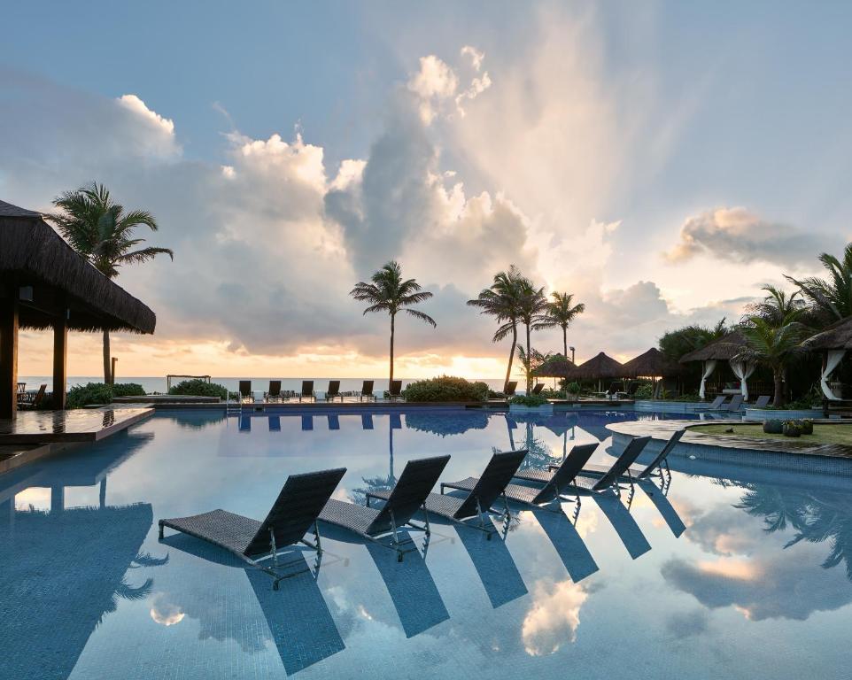 a pool with chairs and palm trees and a sunset at Zorah Beach Hotel in Trairi
