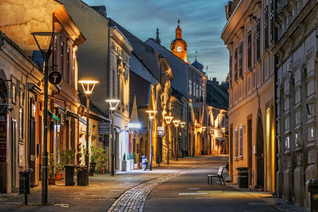 une rue vide la nuit avec une tour d'horloge dans l'établissement Ferencesek apartman, à Pécs