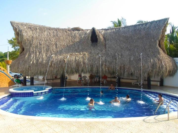un grupo de personas en una piscina con una cabaña de paja en Cabañas La Fragata en Coveñas