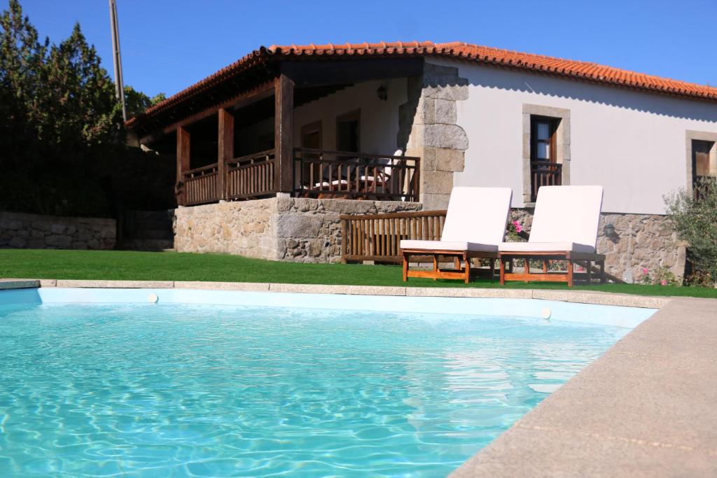 una casa con piscina y 2 sillas blancas en Casa Dona Urraca en Vilarinho da Castanheira