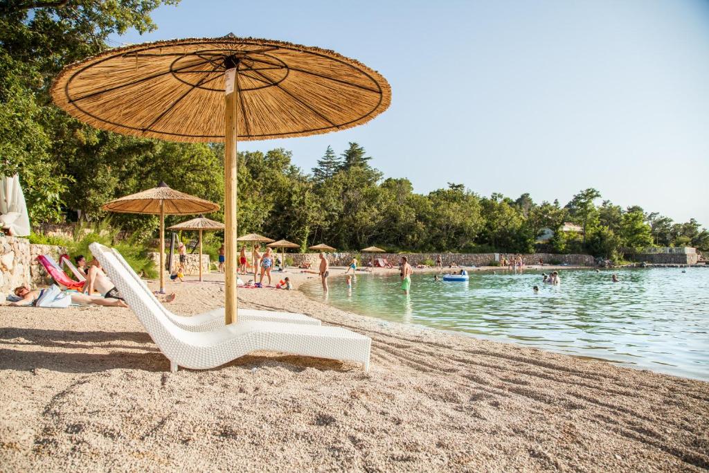 einen Strand mit Sonnenschirm und Stühlen und Menschen im Wasser in der Unterkunft Krk Mobile Homes in Klimno