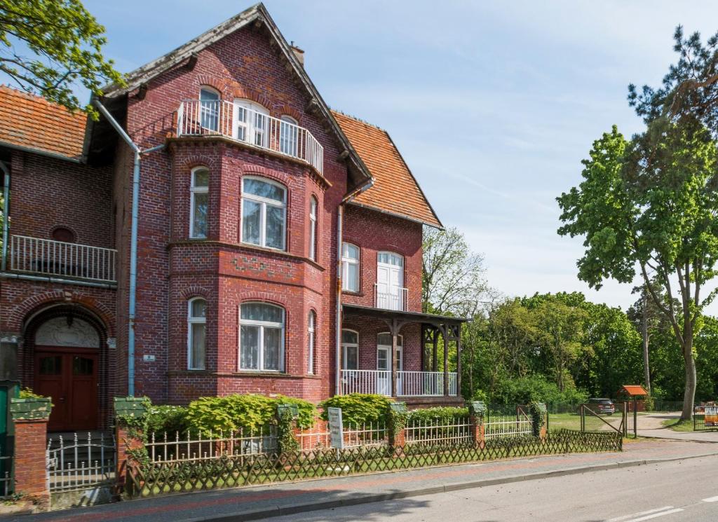 une maison en briques rouges avec une clôture devant elle dans l'établissement Willa "Hel", à Krynica Morska