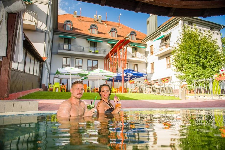 a man and woman sitting in a swimming pool at Hotel Kamilla in Balmazújváros