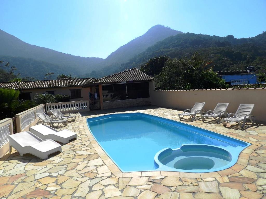 a swimming pool with chairs and a patio with mountains at Pousada Atlantica Recanto do Mar in Caraguatatuba