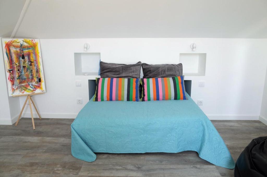 a bed with a blue comforter and a painting at Lisbon Beach Apartments 6 in Costa da Caparica