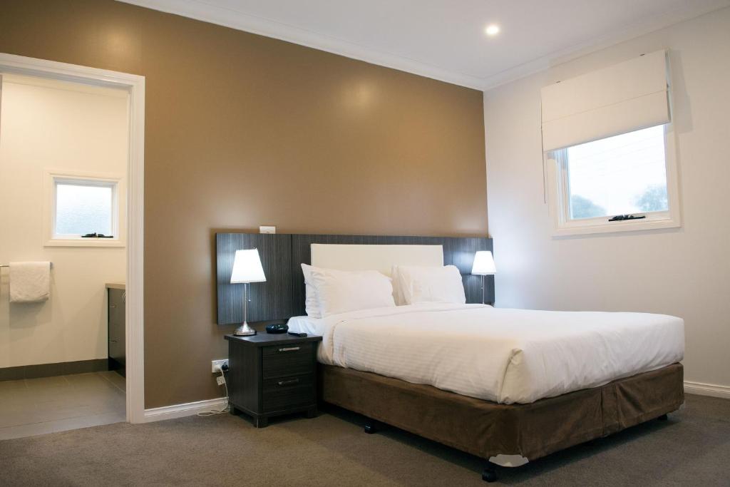 a bedroom with a large bed and two windows at Buckingham Apartments in Highett