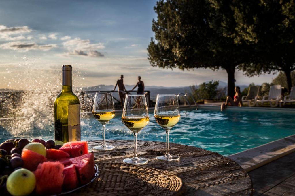 トルジャーノにあるIl Poggio Delle Ginestreのスイミングプールの近くのテーブルに置かれたワインとフルーツ(グラス3杯)