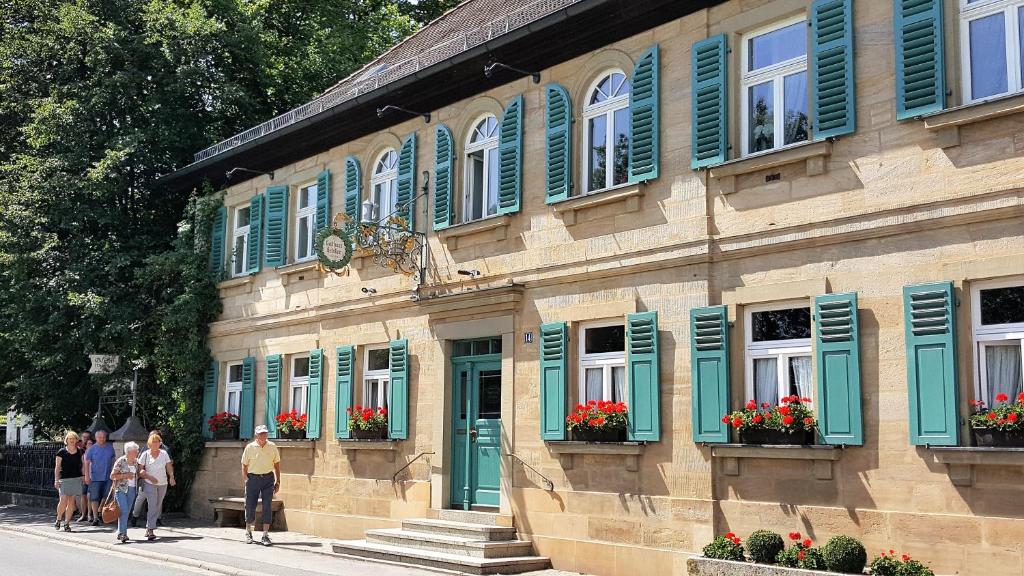 un edificio con persianas verdes y gente caminando delante de él en Gasthof Schiller bei Bamberg, en Strullendorf