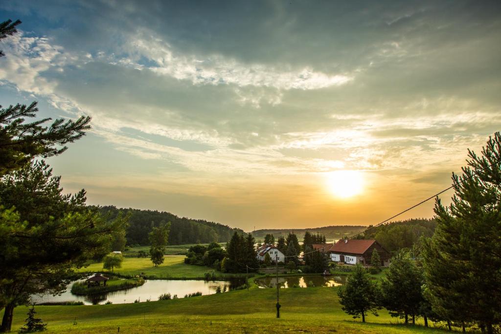 einen Sonnenuntergang über einem Feld mit einem Haus und einem Fluss in der Unterkunft Warmińska Winnica in Barczewo