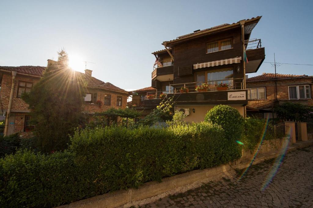 um edifício com o sol no céu atrás de alguns arbustos em Family Hotel Emilia em Sozopol