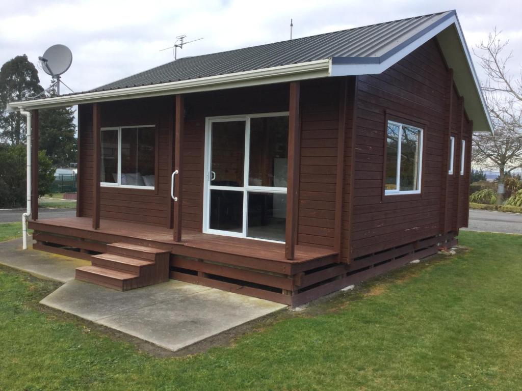a small wooden cabin with a porch and grass at Kairaki Beach Motor Camp in Wetheral