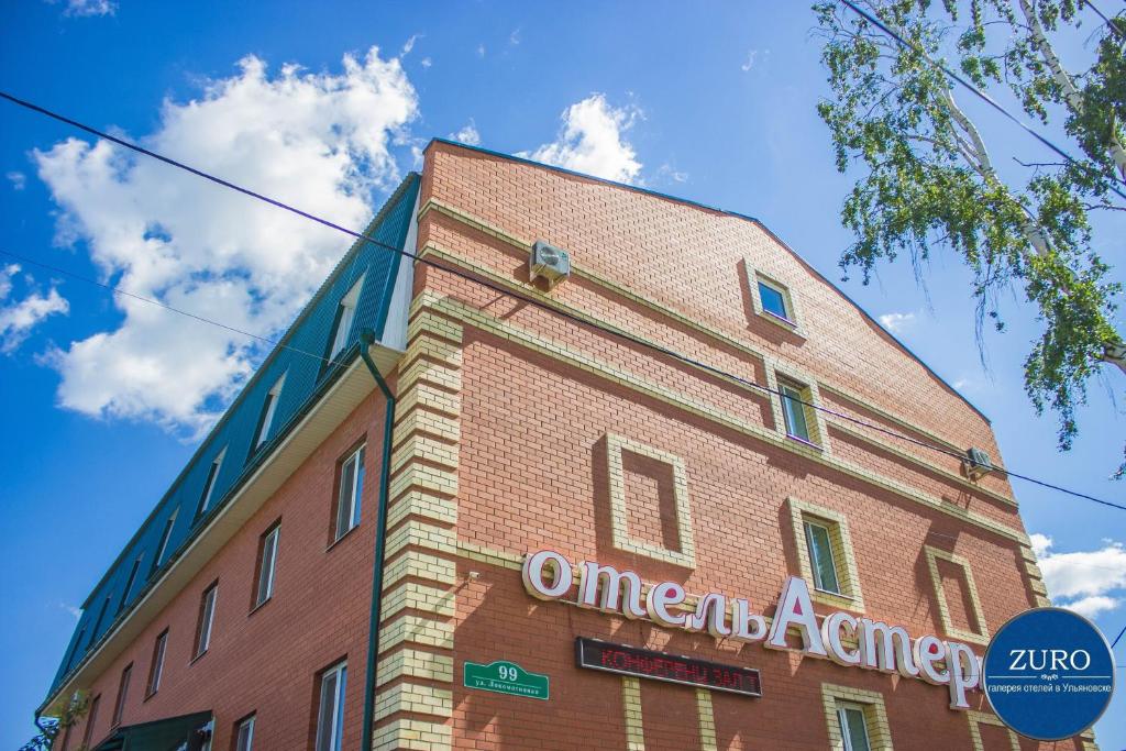 a tall red brick building with a sign on it at Aster Hotel-ZURO in Ulyanovsk