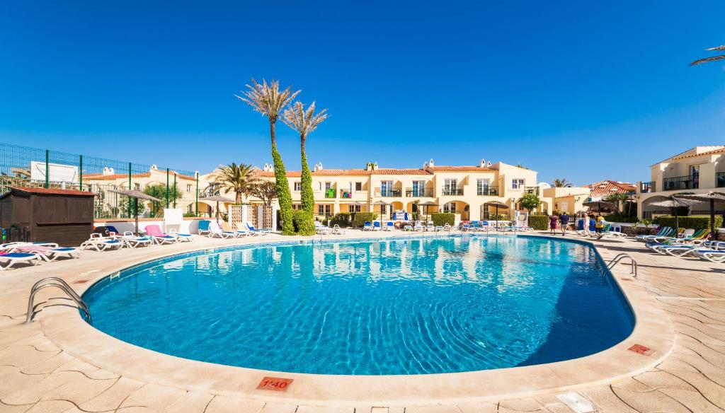 a swimming pool in a resort with chairs and palm trees at Globales Binimar in Cala en Blanes