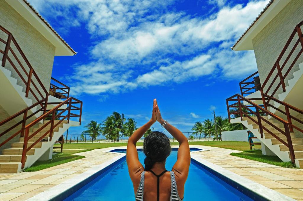 a woman sitting in a swimming pool with her hands in the air at Manga Verde Beach Residence in Itamaracá