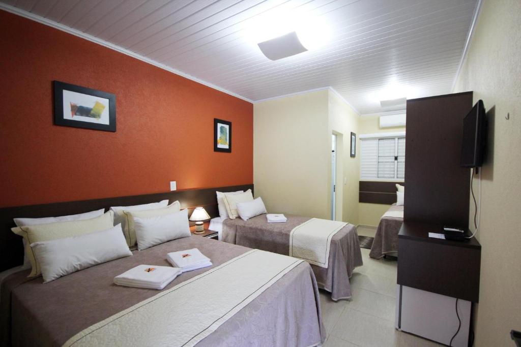 a hotel room with two beds and a flat screen tv at Pousada Recanto Solar dos Pássaros in Olímpia