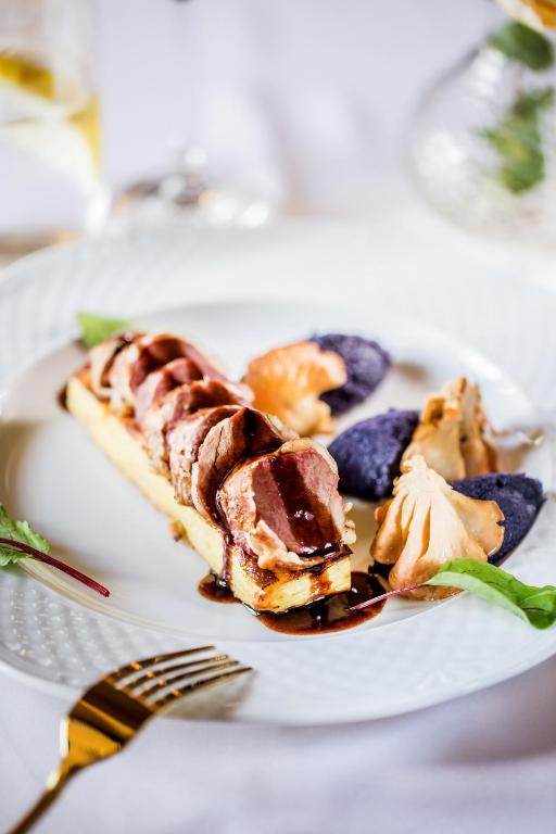 Gourmet plated main course featuring sliced meat, sauce, and colorful vegetable purées