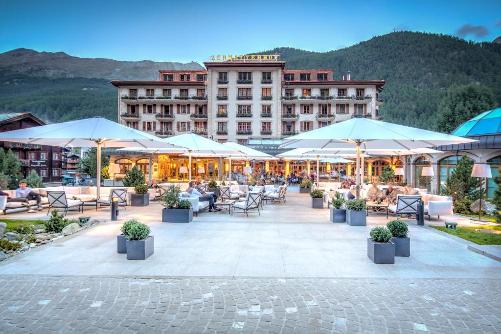 ein Hotel mit einer Terrasse mit Tischen und Sonnenschirmen in der Unterkunft Grand Hotel Zermatterhof in Zermatt