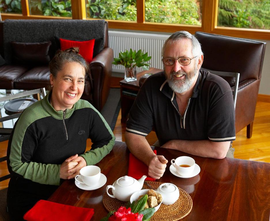 a man and woman sitting at a table with cups of coffee at Kowhai Lane Lodge in Half-moon Bay