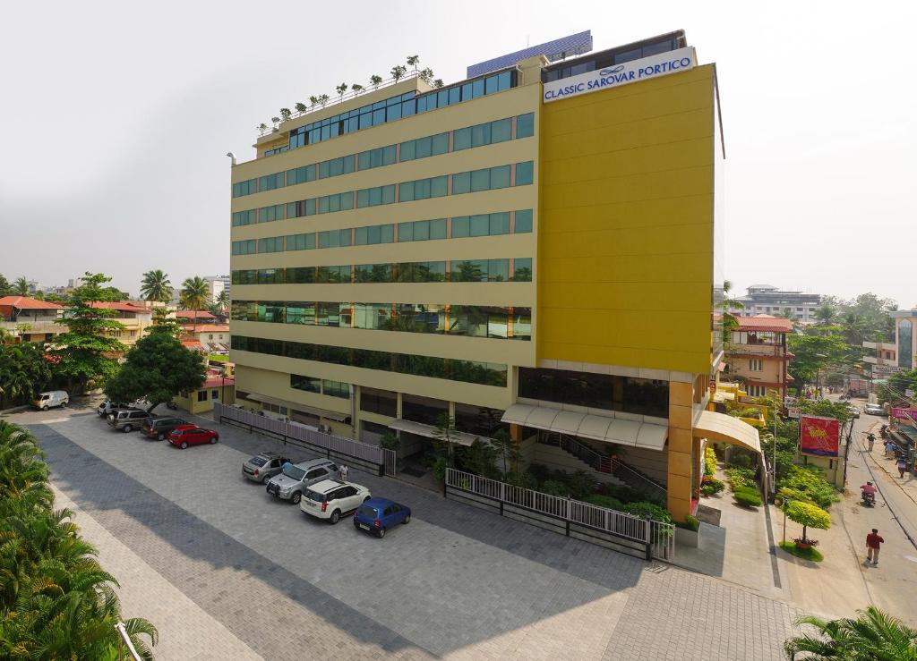 un edificio amarillo con coches estacionados en un estacionamiento en Classic Sarovar Portico Trivandrum, en Trivandrum