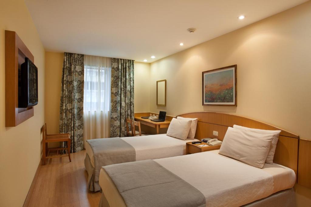 a hotel room with two beds and a desk at Windsor Martinique Copacabana in Rio de Janeiro