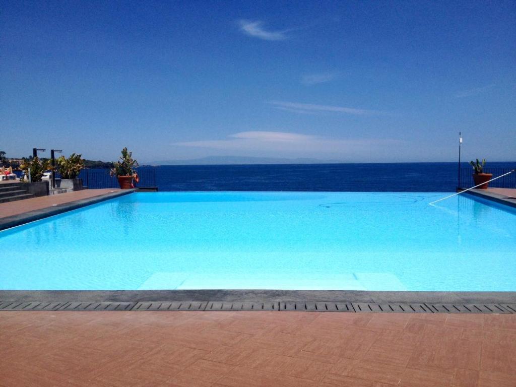 a large blue swimming pool with the ocean in the background at Santa Tecla Palace in Acireale