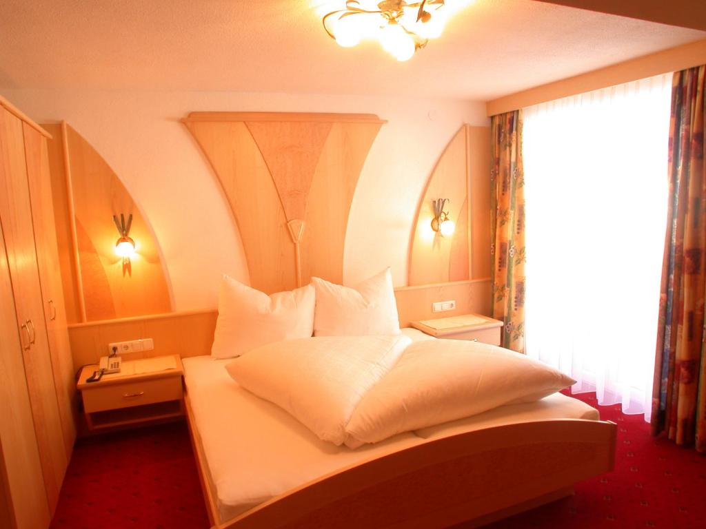 a bedroom with a bed with white sheets and a window at Hotel Garni Pradella in Ischgl