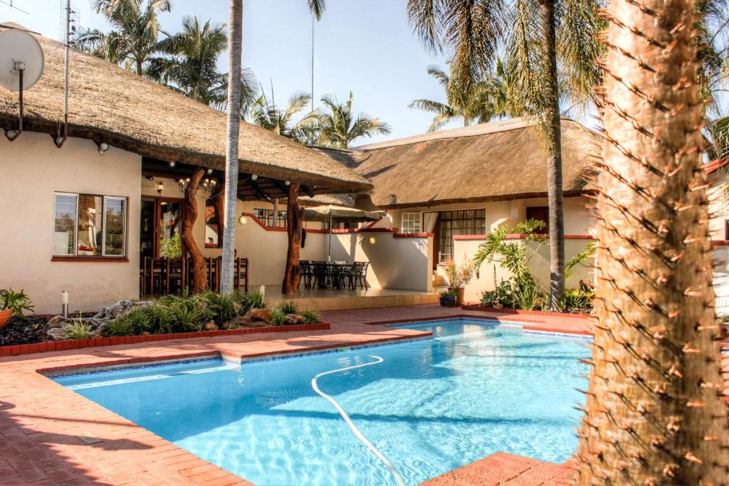 a swimming pool in front of a house with a palm tree at Marlot Guest House in Polokwane