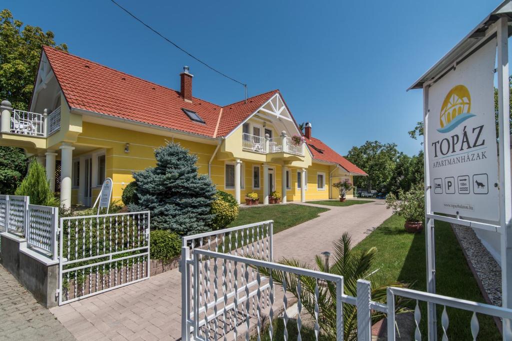 ein gelbes Haus mit einem Schild davor in der Unterkunft Topáz Apartmanházak in Balatongyörök