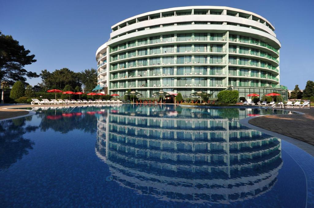 a large building with a reflection in a pool of water at Hotel Colosseum in Sunny Beach
