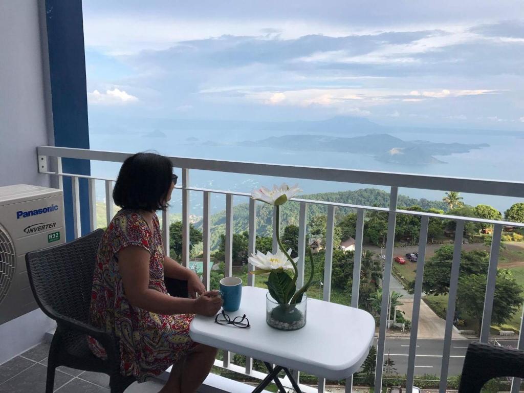 una mujer sentada en una mesa en un balcón en Taal View Condo by Liza en Tagaytay