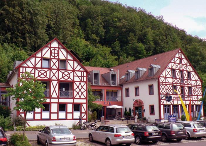 un groupe de bâtiments avec des voitures garées dans un parking dans l'établissement Behringers Freizeit - und Tagungshotel, à Gößweinstein