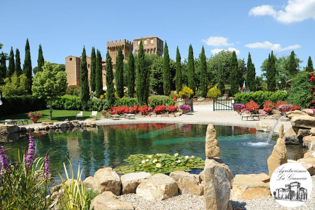 a garden with a pond with flowers and a building at Agriturismo Castello La Grancia di Spedaletto in Pienza