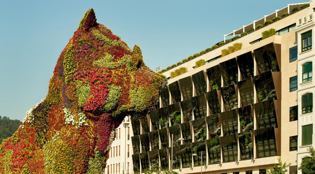 a sculpture of a dog covered in flowers in front of a building at The Artist Grand Hotel of Art in Bilbao