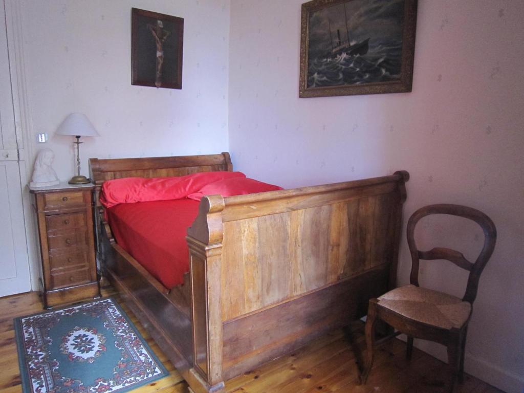 a bedroom with a wooden bed with red sheets and a chair at La Maison de Mireille in Le Puy-en-Velay