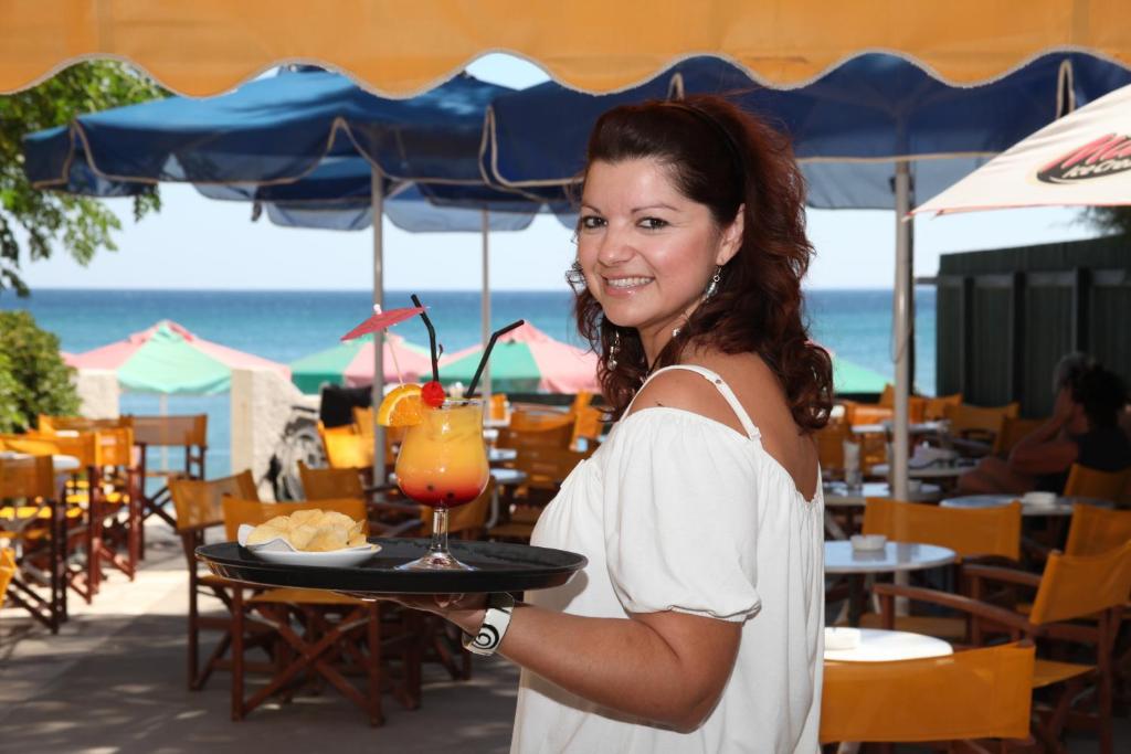 a woman holding a tray of food and a drink at Hydrele Beach Hotel & Village in Potokáki