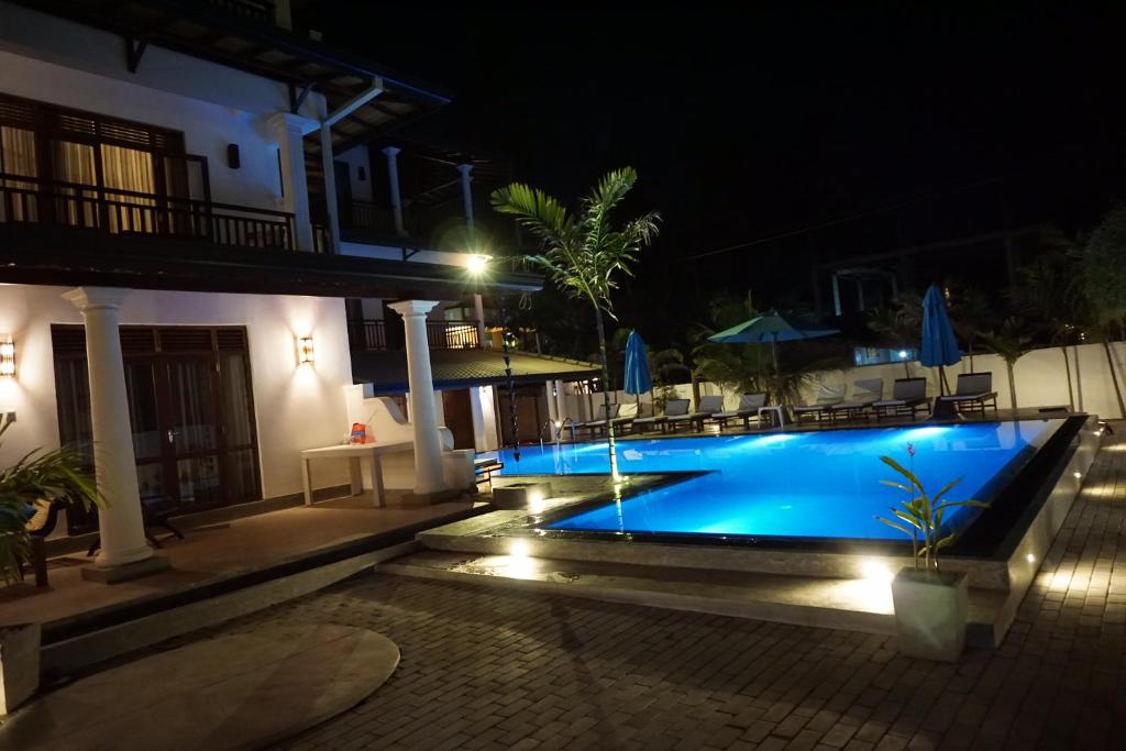 una piscina por la noche con sillas y sombrillas en Malee Villa (Beach Inns Holiday Resort) en Matara