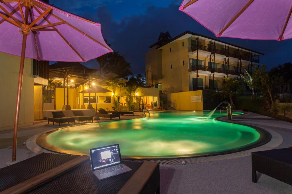 a swimming pool with an umbrella and a laptop on a table at Mountain Creek Wellness Resort Chiangmai in Chiang Mai