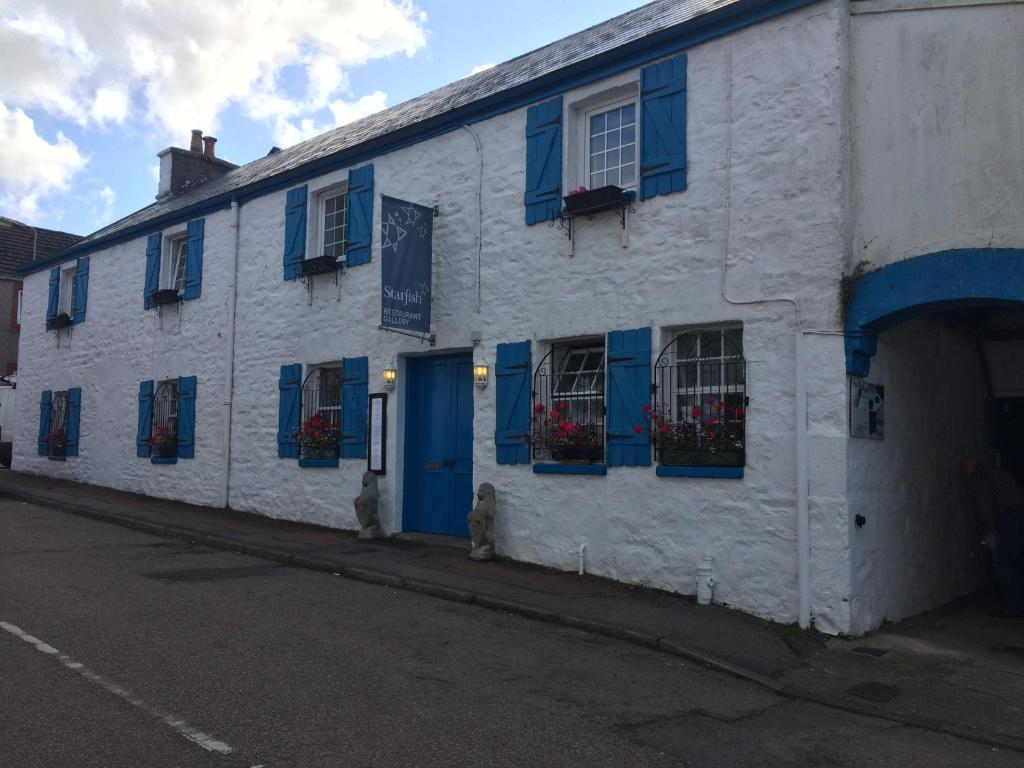 a white building with blue shutters on a street at Starfish Rooms in Tarbert