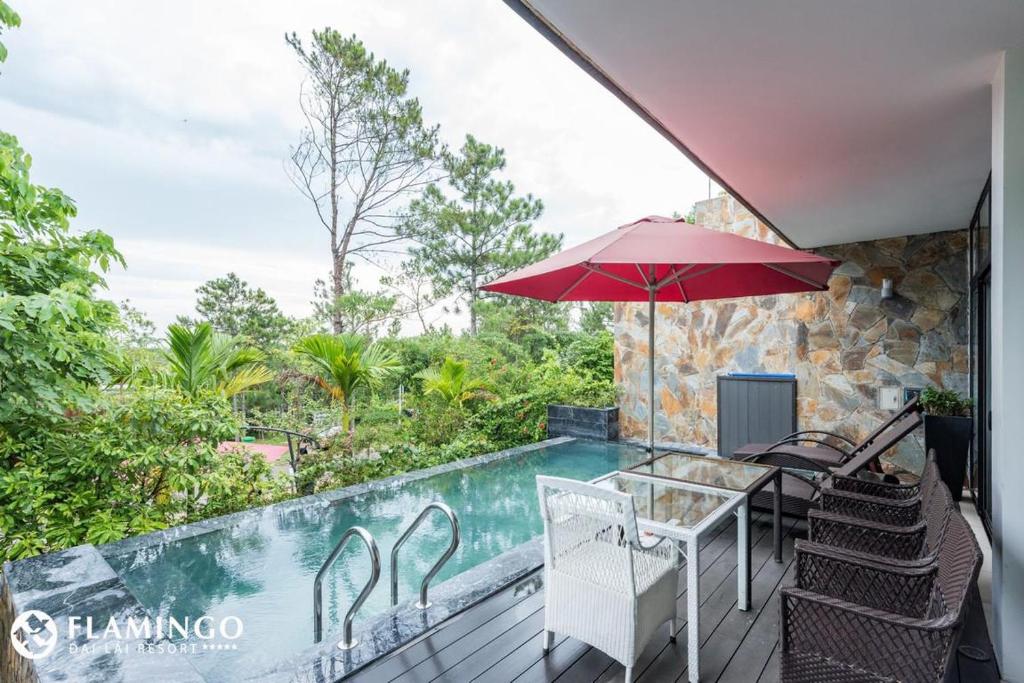 a patio with a table and umbrella and a swimming pool at FLAMINGOS Villa Happy BT in Ngọc Quang