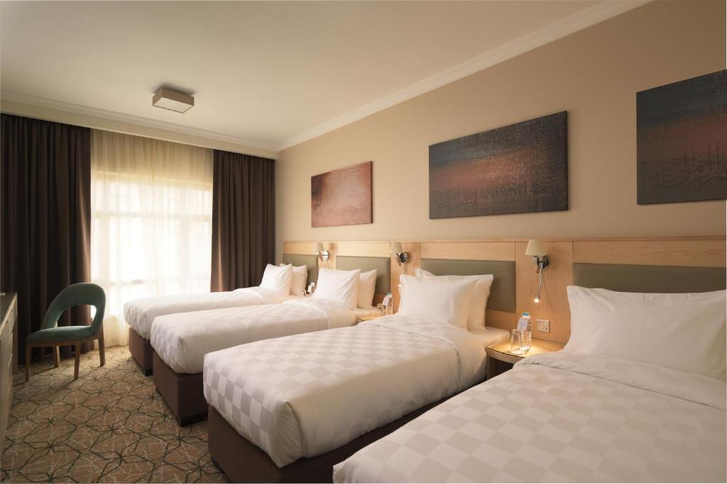 a hotel room with three beds and a chair at Saja Al Madinah in Al Madinah