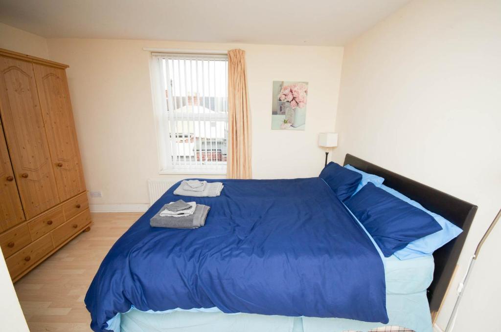 a bedroom with a bed with blue sheets and a window at MARLEY MANSIONs APARTMENT - CLARENDON in Wallasey