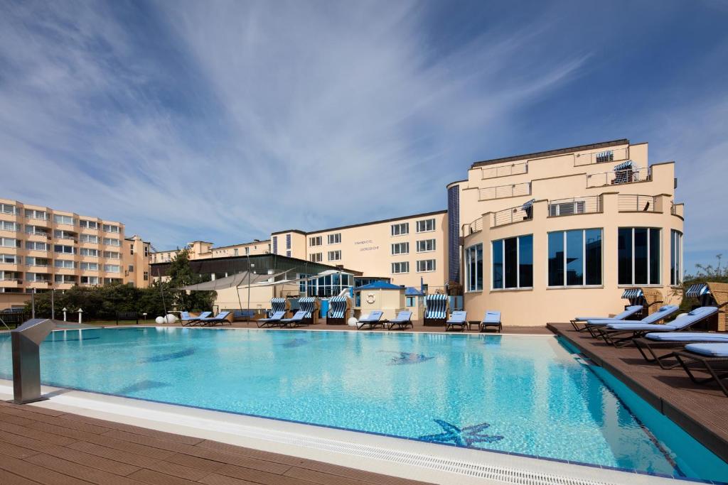 a large swimming pool with lounge chairs next to a building at Strandhotel Georgshöhe in Norderney