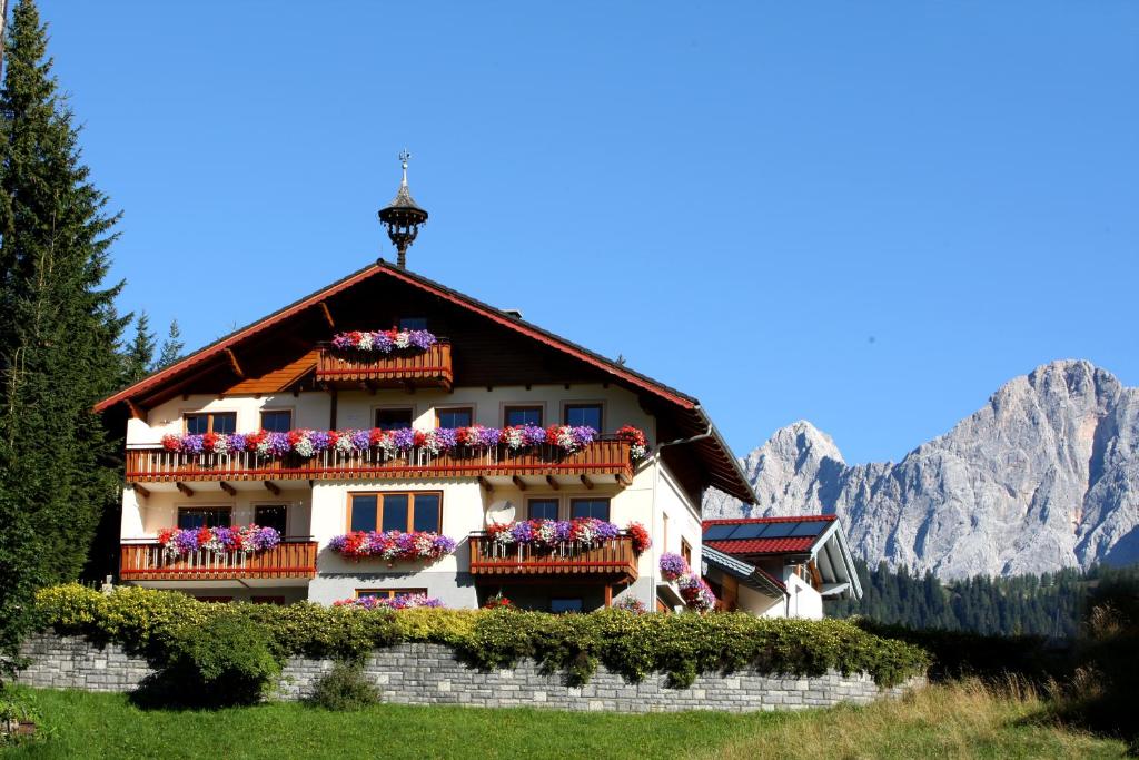 une maison dans les montagnes avec des fleurs sur les balcons dans l'établissement Pension Felsenheim, à Ramsau am Dachstein